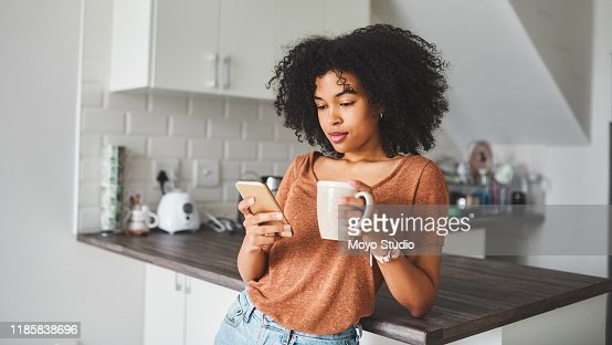 Shot of a young woman using a smartphone and having coffee in the kitchen at home