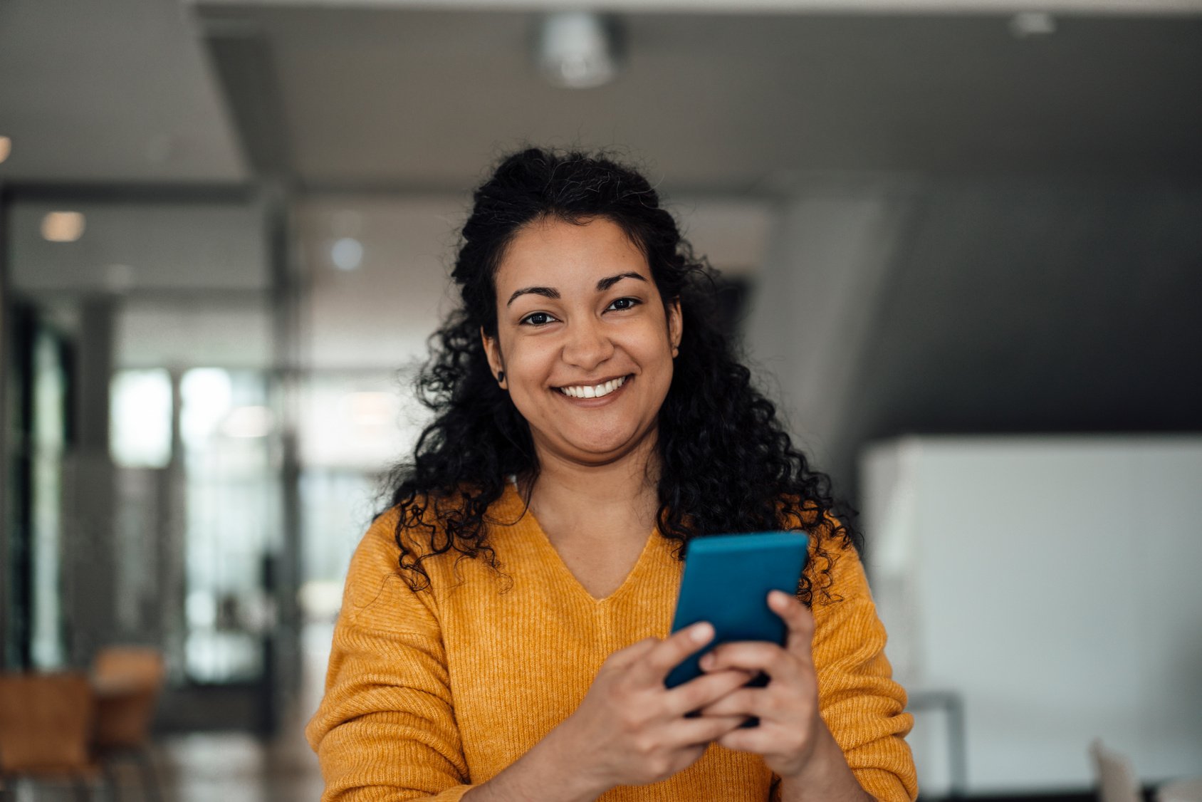 Happy businesswoman holding smart phone at office