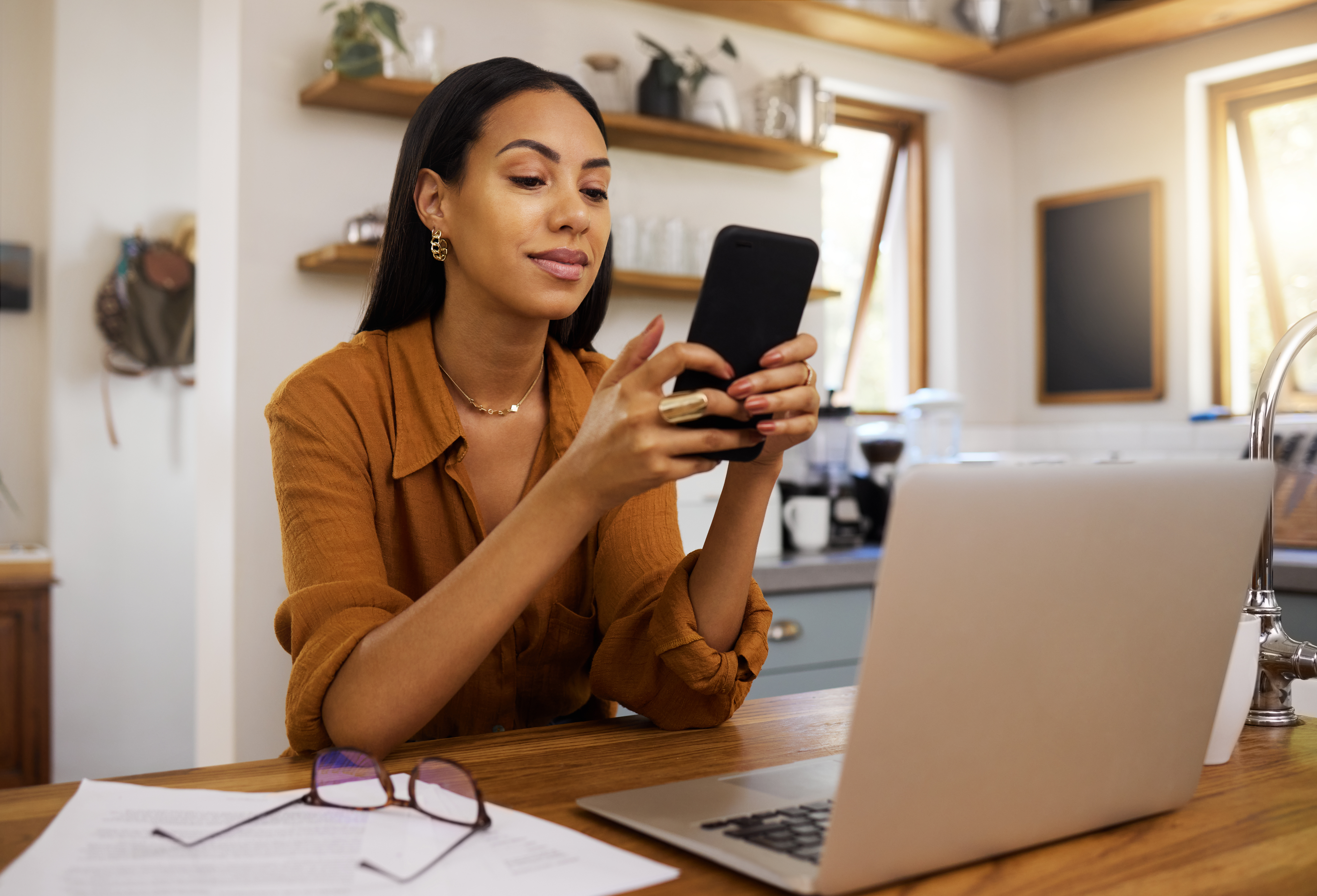 Remote work, phone and texting by business woman in kitchen with laptop, documents and form. Freelance, smartphone and female checking app, website or social media while working on online proposal.