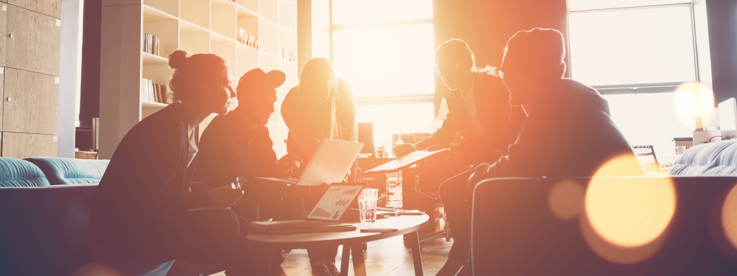 Silhouette of startup business team. Meeting on the couch. Big open space office. Five people. Intentional sun glare and lens flares. Wide screen, panoramic