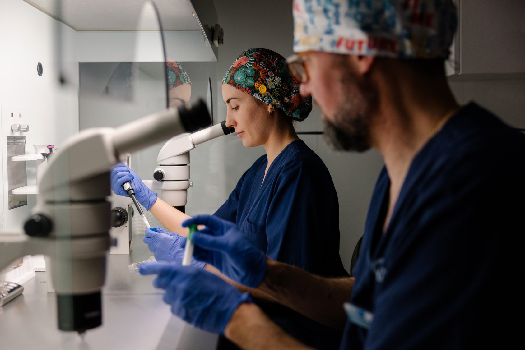 Two professional biologists are focused on laboratory work, using a microscope to analyze samples.
